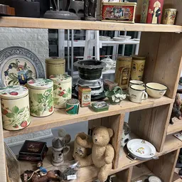Houten stellingkast met verzameling vintage huishoudartikelen: bloemmotief blikken, keramische potten, kopjes en decoratieve 