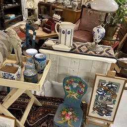 Uitgestalde tweedehands meubels en decoratiestukken inclusief witte kast, blauwe kruk, aardewerk en kunstobjecten