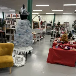Winkelvloer met kerstdecoratie, blauwe kunstkerstboom, rode tafels met kerstspullen en gele fauteuil