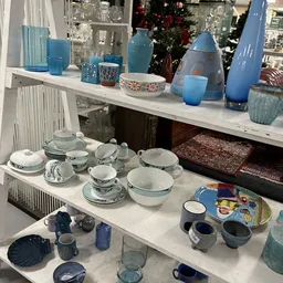 Uitgestalde serviesgoed en huishoudartikelen op witte toonbanken in kringloopwinkel