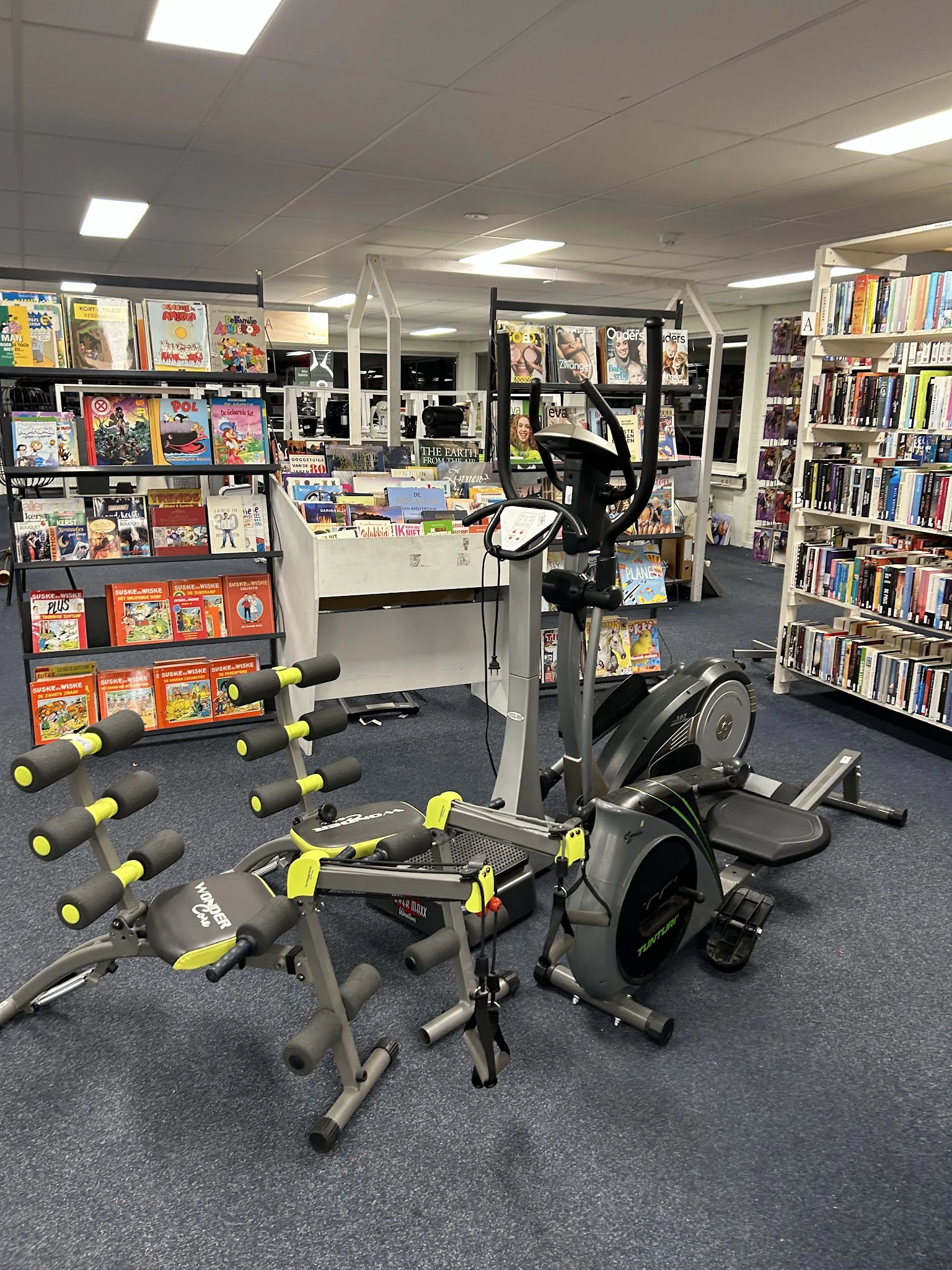 Fitnessapparatuur en halters in een winkelruimte met boekenkasten en media op de achtergrond