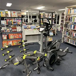 Fitnessapparatuur en halters in een winkelruimte met boekenkasten en media op de achtergrond