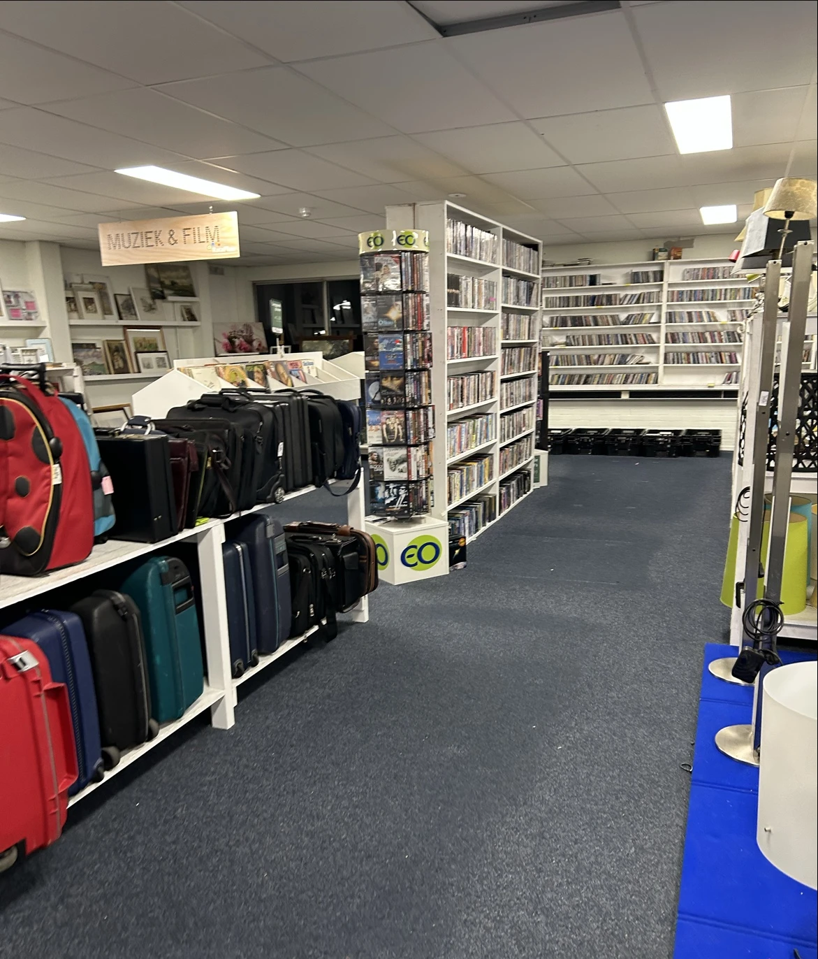 Winkelinterieur met stellingen vol cd's en dvd's, koffers en tassen op display, en een muziek- en filmafdeling