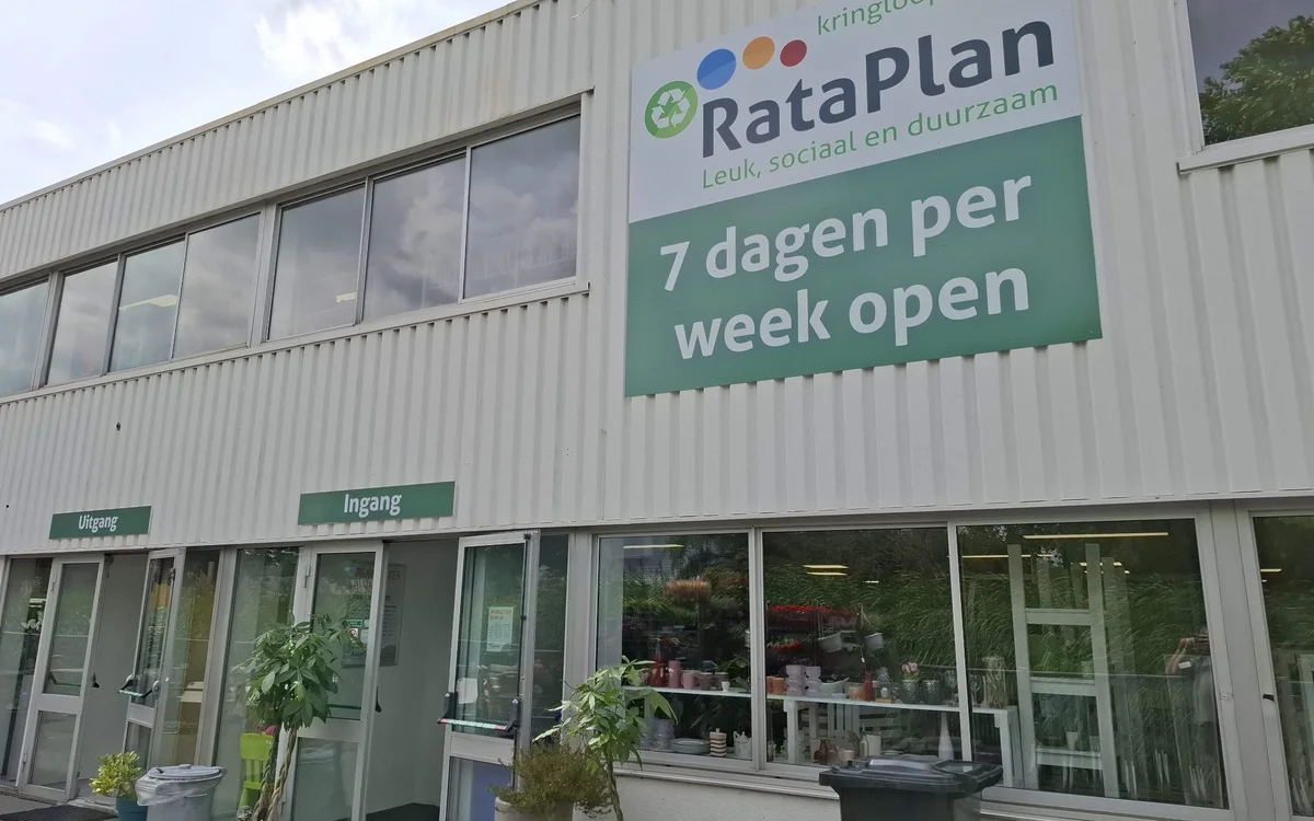 Voorgevel van kringloopwinkel RataPlan met groene en witte signage, twee ingangsdeuren en ramen, met informatie '7 dagen per 