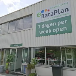 Voorgevel van kringloopwinkel RataPlan met groene en witte signage, twee ingangsdeuren en ramen, met informatie '7 dagen per 