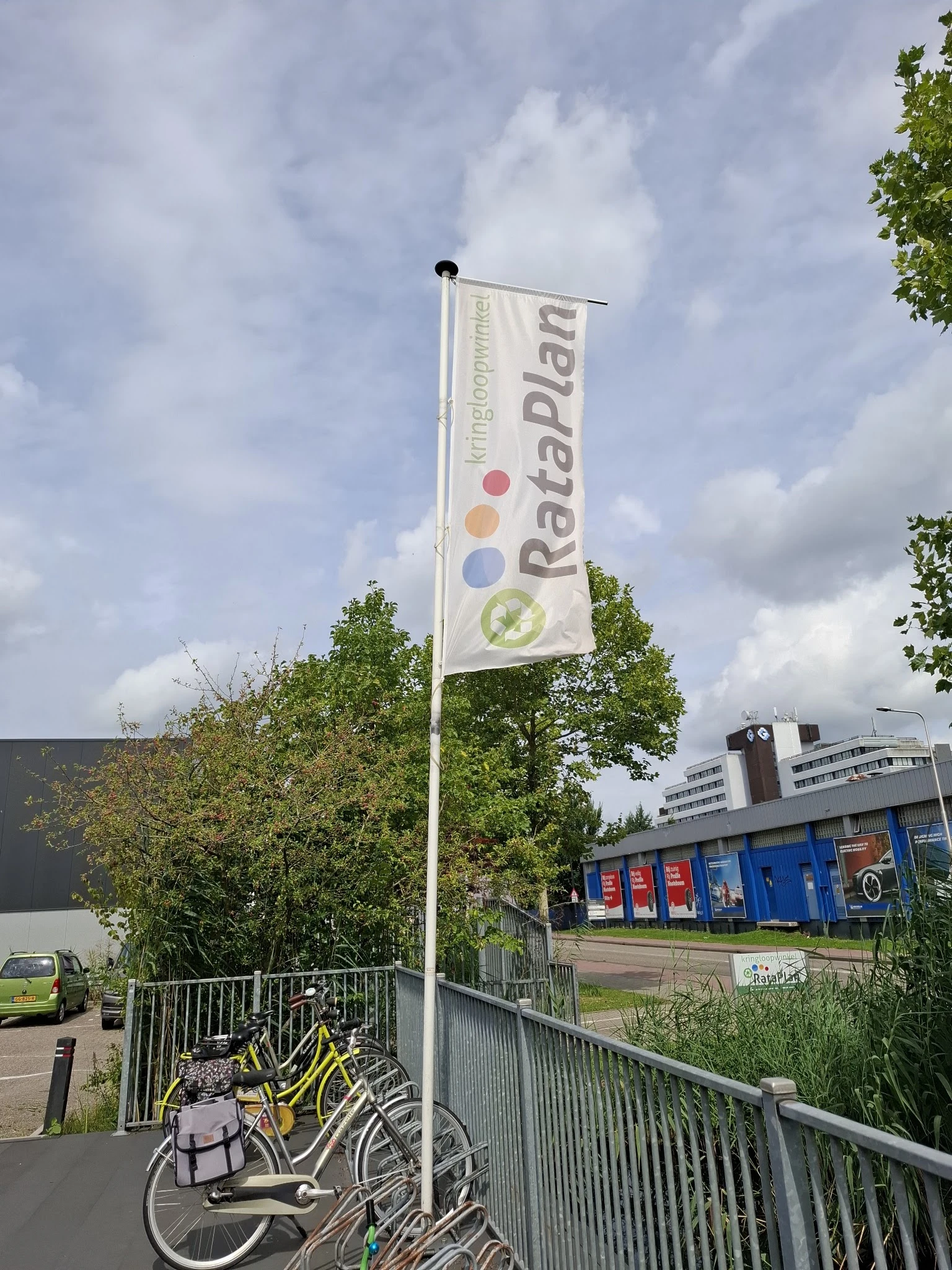 Voorkant kringloopwinkel met blauw-rode deuren en Rataplan-vlag met logo