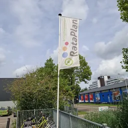 Voorkant kringloopwinkel met blauw-rode deuren en Rataplan-vlag met logo