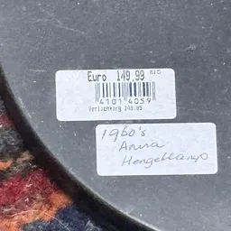Twee prijsstickers op donkere ondergrond: één met barcode en 'Euro 109.99', één met handgeschreven '1960's Aura Hengelmann'