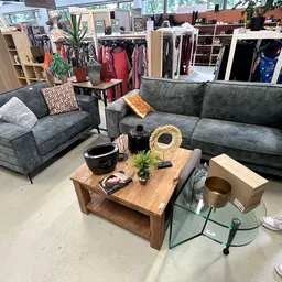 Showroom met twee grijze banken, houten salontafel en kledingrekken met kleding op de achtergrond