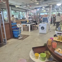 Winkelvloer met wasmachine, blauwe kratten, kleding op rekken en diverse huishoudelijke spullen