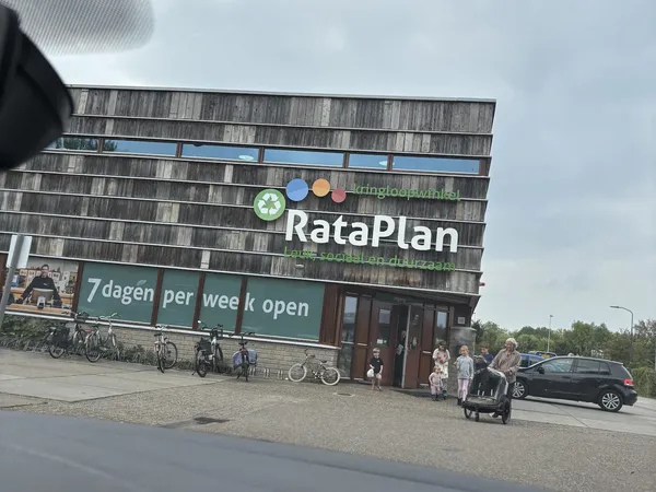 Gevel van RataPlan kringloopwinkel met groene banner, fietsen ervoor geparkeerd en bezoekers op het plein