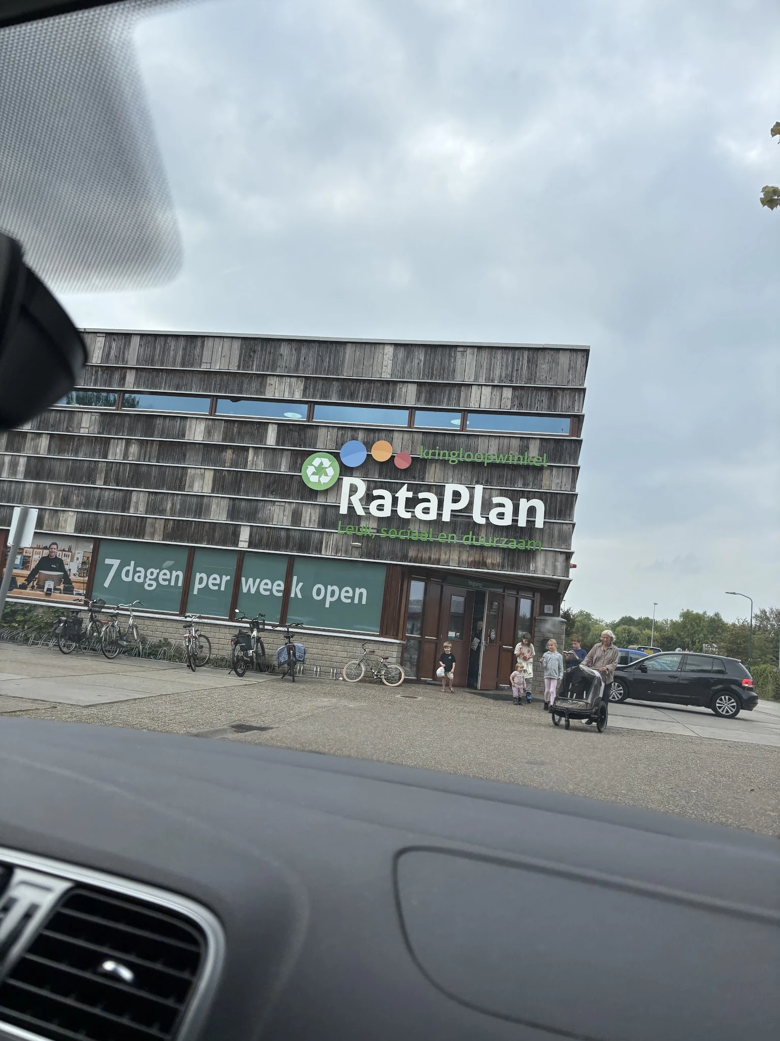 Gevel van RataPlan kringloopwinkel met groene banner, fietsen ervoor geparkeerd en bezoekers op het plein