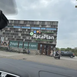 Gevel van RataPlan kringloopwinkel met groene banner, fietsen ervoor geparkeerd en bezoekers op het plein