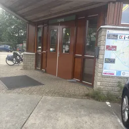 Ingang van kringloopwinkel met bruine deuren, zwarte deurmat en winkelramen aan de voorgevel