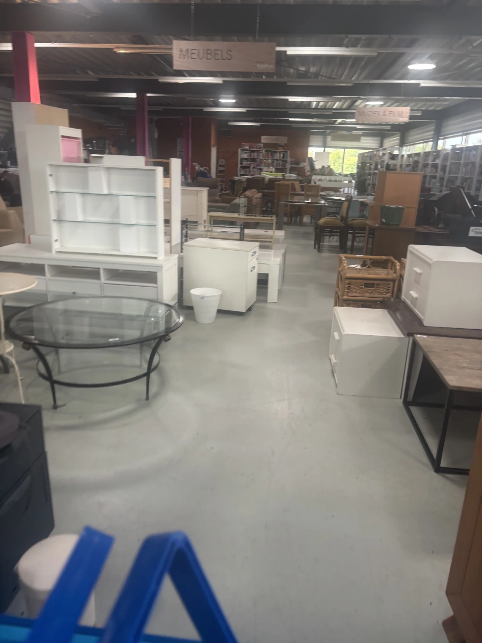 Winkelvloer met uitgestalde meubels: glazen salontafel, witte kasten, houten tafels en andere meubelstukken