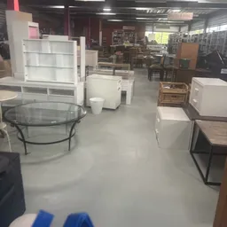 Winkelvloer met uitgestalde meubels: glazen salontafel, witte kasten, houten tafels en andere meubelstukken