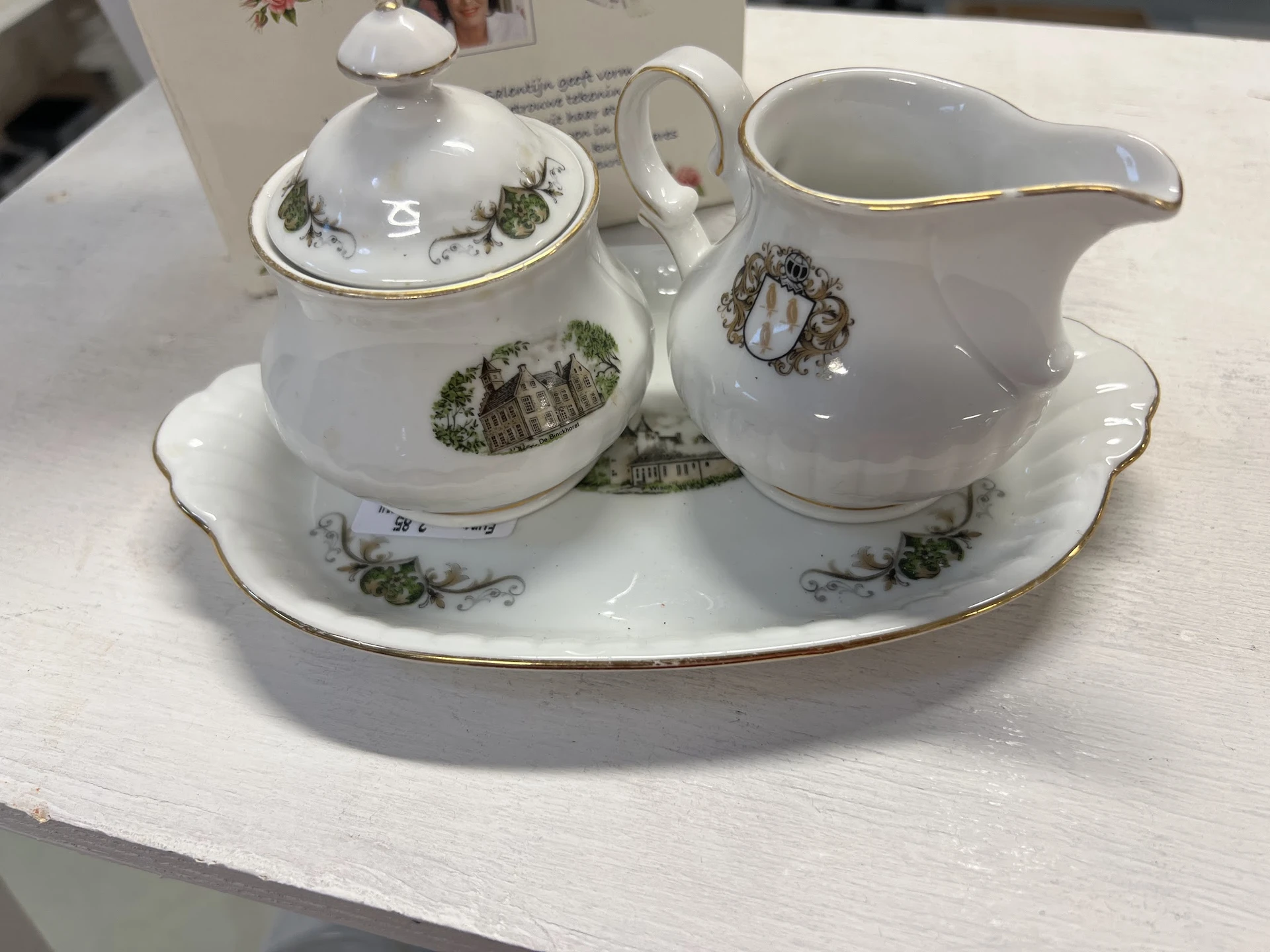 Wit porselein servies met groen decor: suikerpot met deksel, melkkan en onderschotel op ovale schotel met goudrand