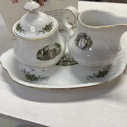 Wit porselein servies met groen decor: suikerpot met deksel, melkkan en onderschotel op ovale schotel met goudrand