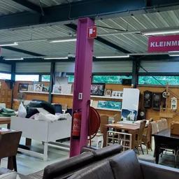 Winkelvloer met meubels, stellingen, en verschillende afdelingen in een ruime kringloopwinkel