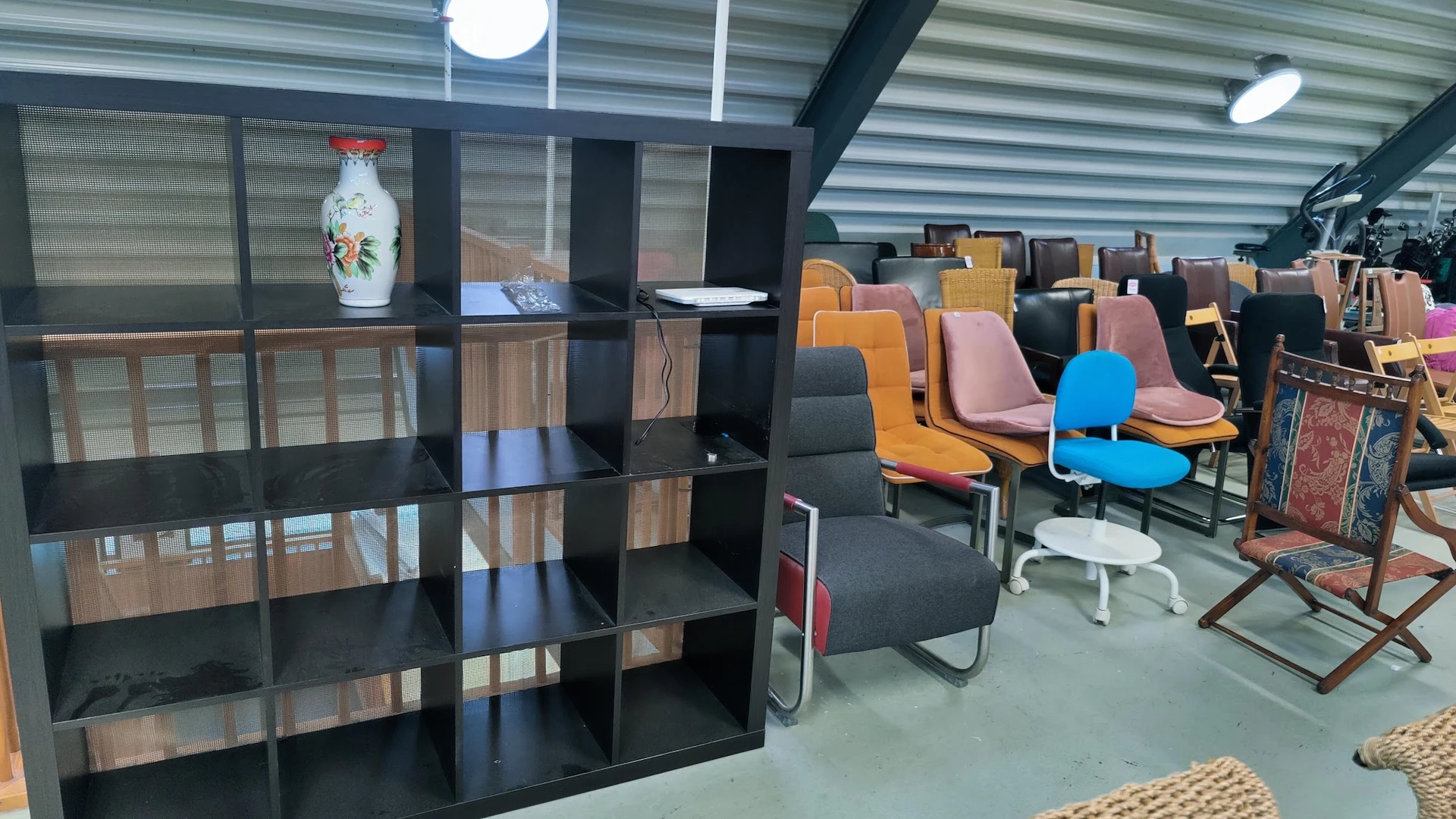 Winkelvloer met zwart stellingkast op de voorgrond en diverse gekleurde stoelen en fauteuils op de achtergrond