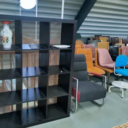 Winkelvloer met zwart stellingkast op de voorgrond en diverse gekleurde stoelen en fauteuils op de achtergrond