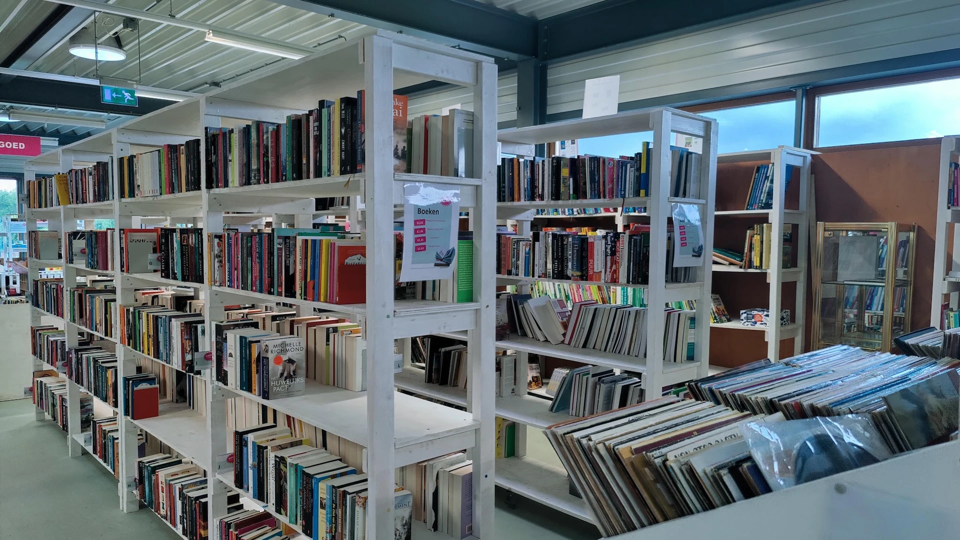 Wit stelling systeem met boeken in een kringloopwinkel, met dvd's en media op de voorgrond.