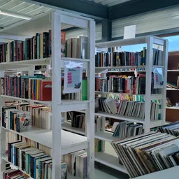 Wit stelling systeem met boeken in een kringloopwinkel, met dvd's en media op de voorgrond.
