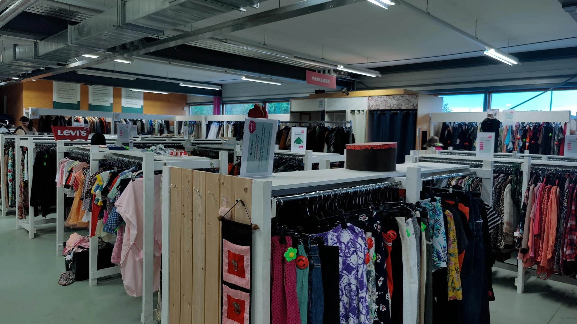 Winkelinterieur met rekken vol tweedehands kleding, witte scheidingswanden en verlichting van bovenaf