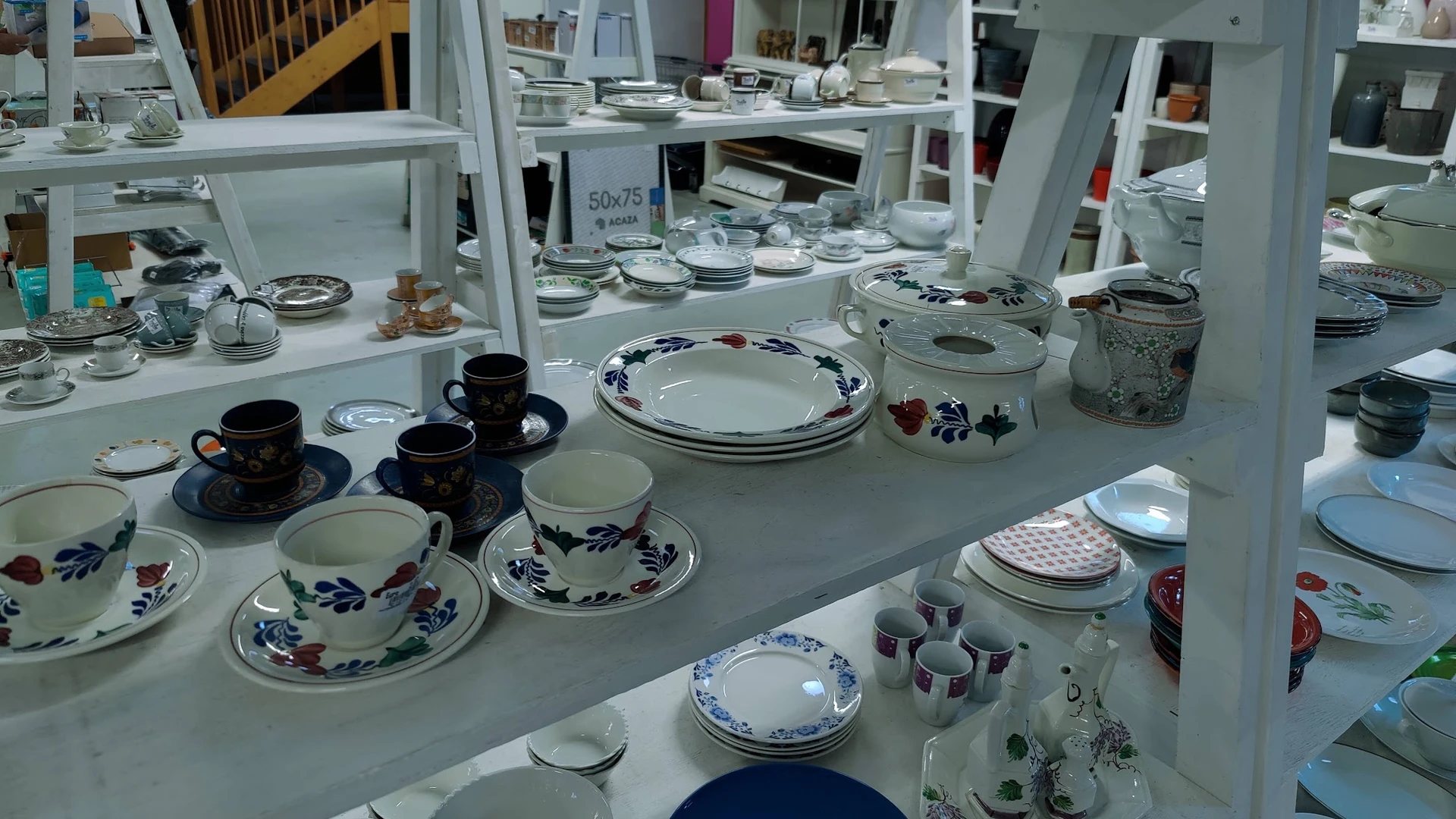 Uitgestalde serviesgoed en porselein met blauwe decoraties op witte toonbanken in de kringloopwinkel