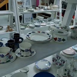 Uitgestalde serviesgoed en porselein met blauwe decoraties op witte toonbanken in de kringloopwinkel