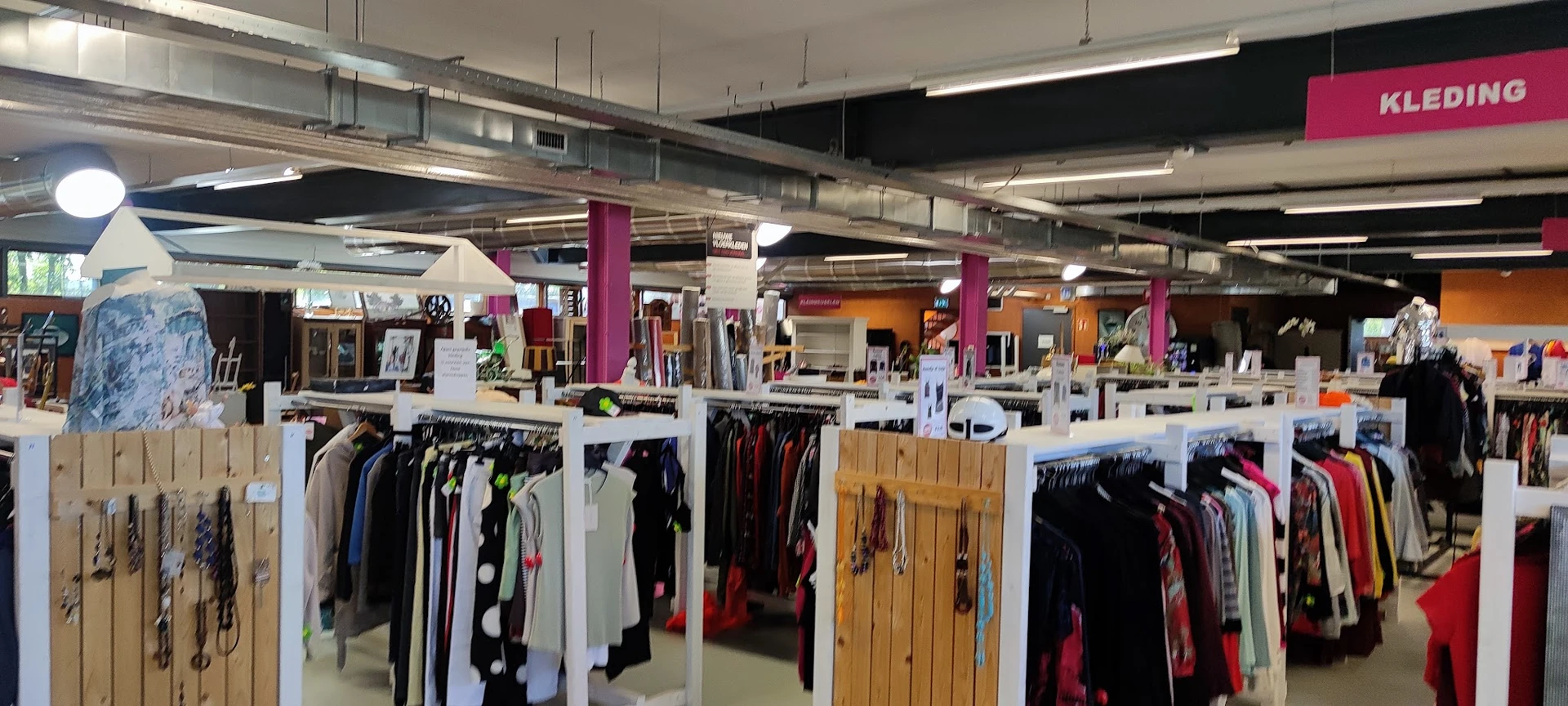 Winkelvloer met kledingrekken en paarse zuilen in een kringloopwinkel