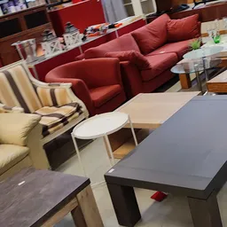 Zithoek met rode fauteuils en witte bijzettafels in kringloopwinkel
