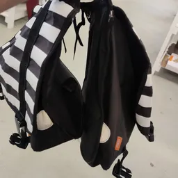 Zwarte rugzak met wit geruit patroon en gekleurde labels, detail van de voorzijde