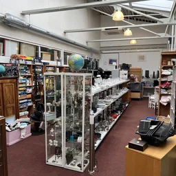 Winkelvloer met glazen vitrines vol collectibles, houten kasten en diverse spullen onder industriële verlichting