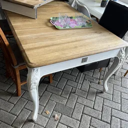 Witte eettafel met licht houten tafelblad en gebogen poten, getoond in showroom.