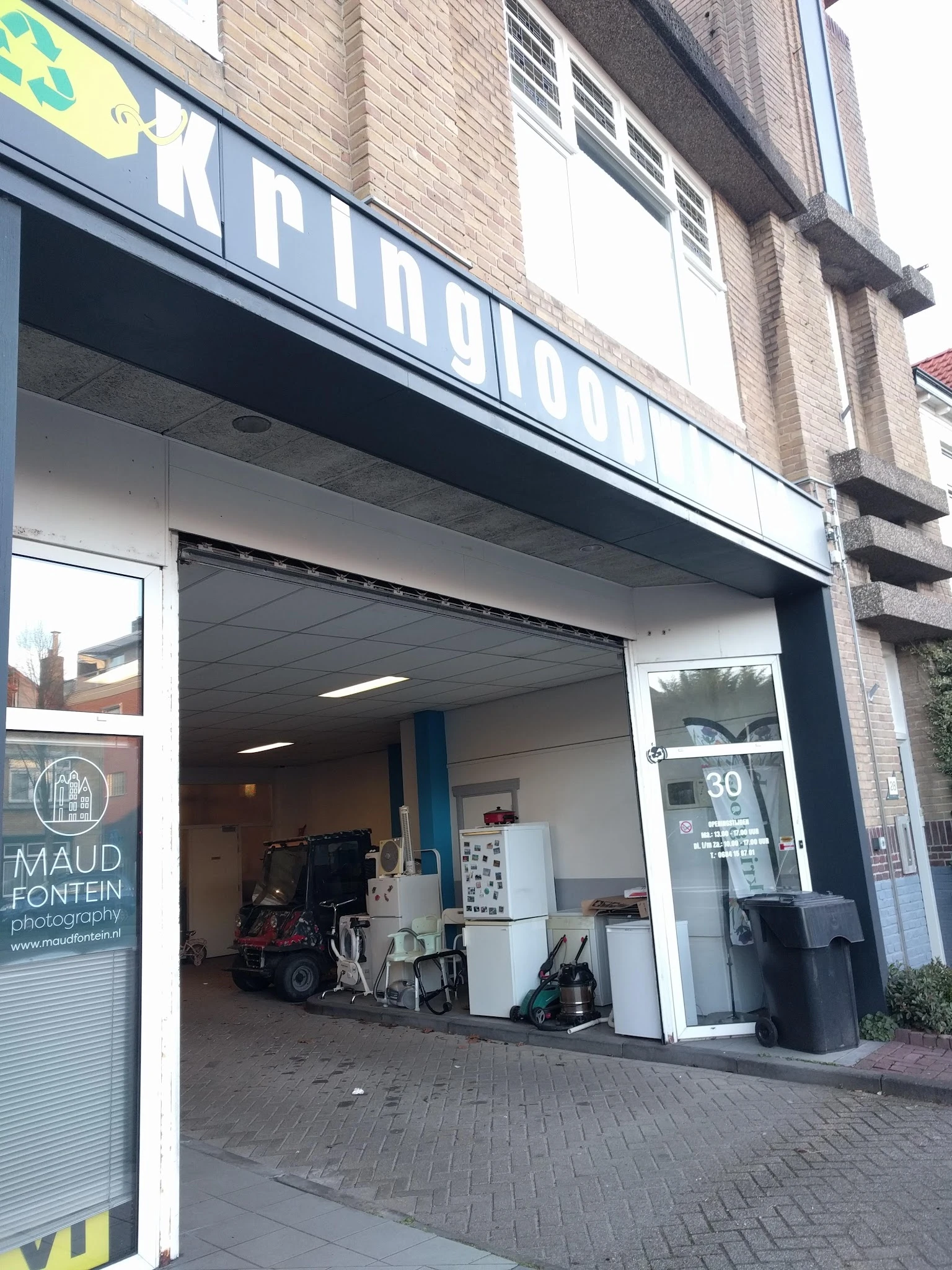 Winkelfront met grote etalageruiten, blauwe kozijnen en huisnummer 30, zicht op verlichting en deel van het interieur