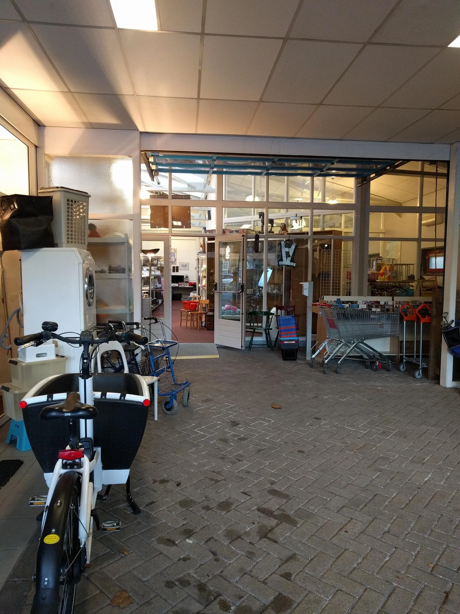Winkelentree met glazen deuren, kinderwagens en spullen op de vloer, zicht op het interieur