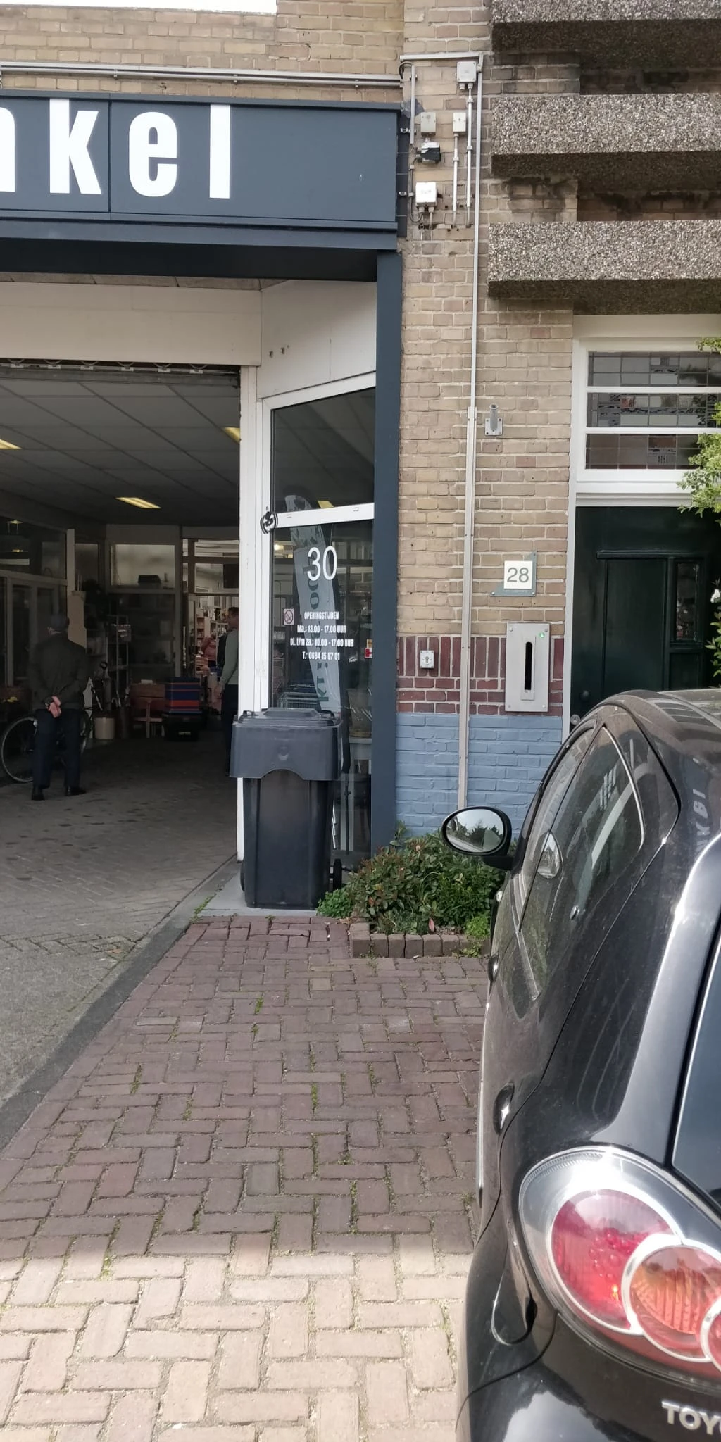 Voorzijde van kringloopwinkel met parkeerautomaat en geparkeerde auto op straat