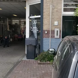 Voorzijde van kringloopwinkel met parkeerautomaat en geparkeerde auto op straat