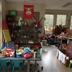 Speelgoedafdeling in kringloopwinkel met speelgoed, poppen, auto's en diverse kinderspullen op tafels en stellingen