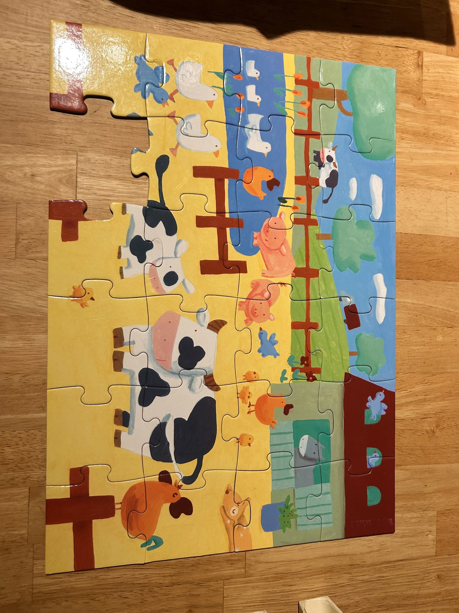 Kleurrijke houten puzzel met boerderijdieren en landschap, gedeeltelijk in elkaar gezet op houten vloer