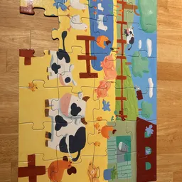 Kleurrijke houten puzzel met boerderijdieren en landschap, gedeeltelijk in elkaar gezet op houten vloer
