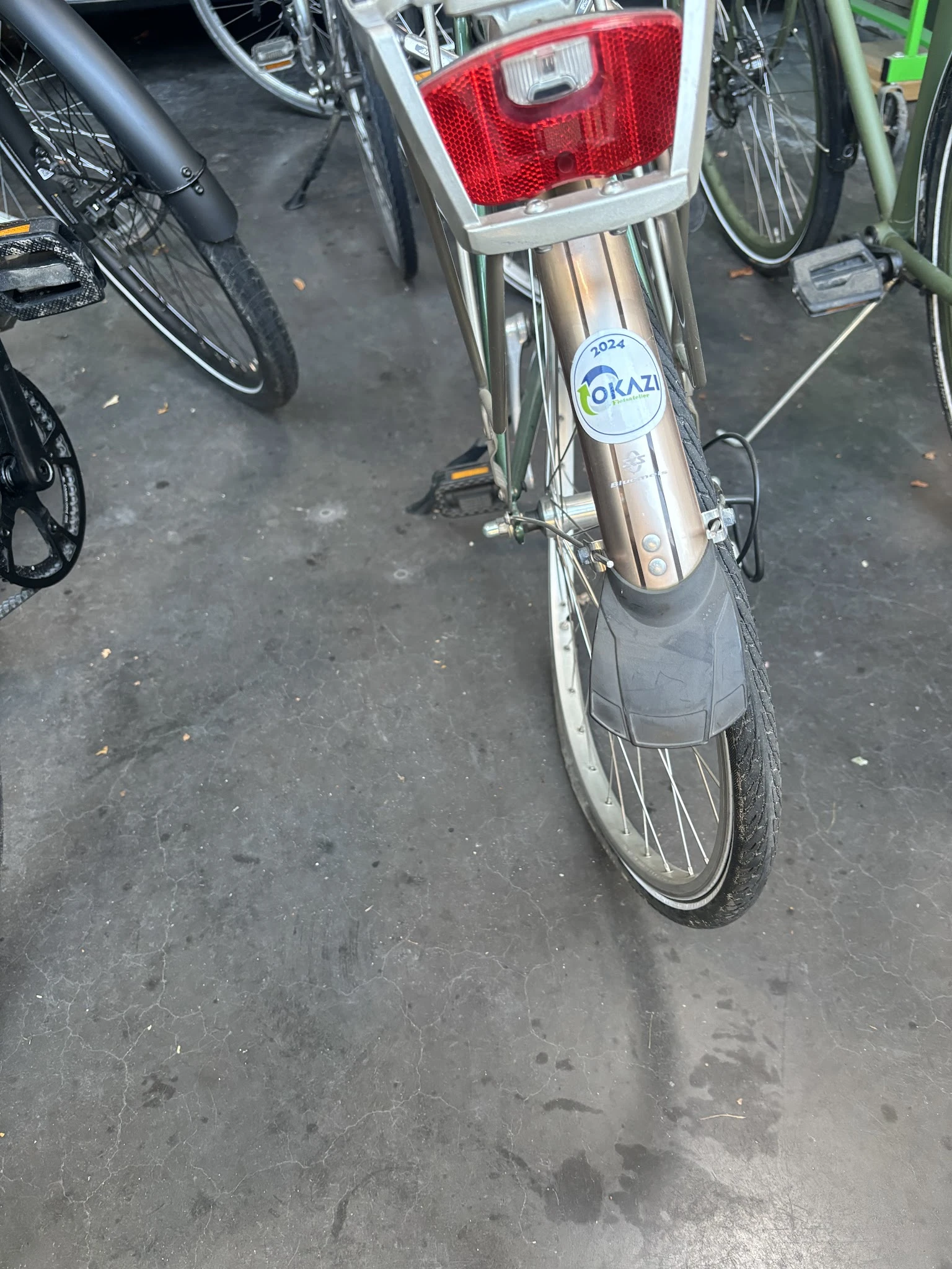 Close-up van een tweedehands fiets met Okazi-sticker op het frame, geparkeerd op asfalt