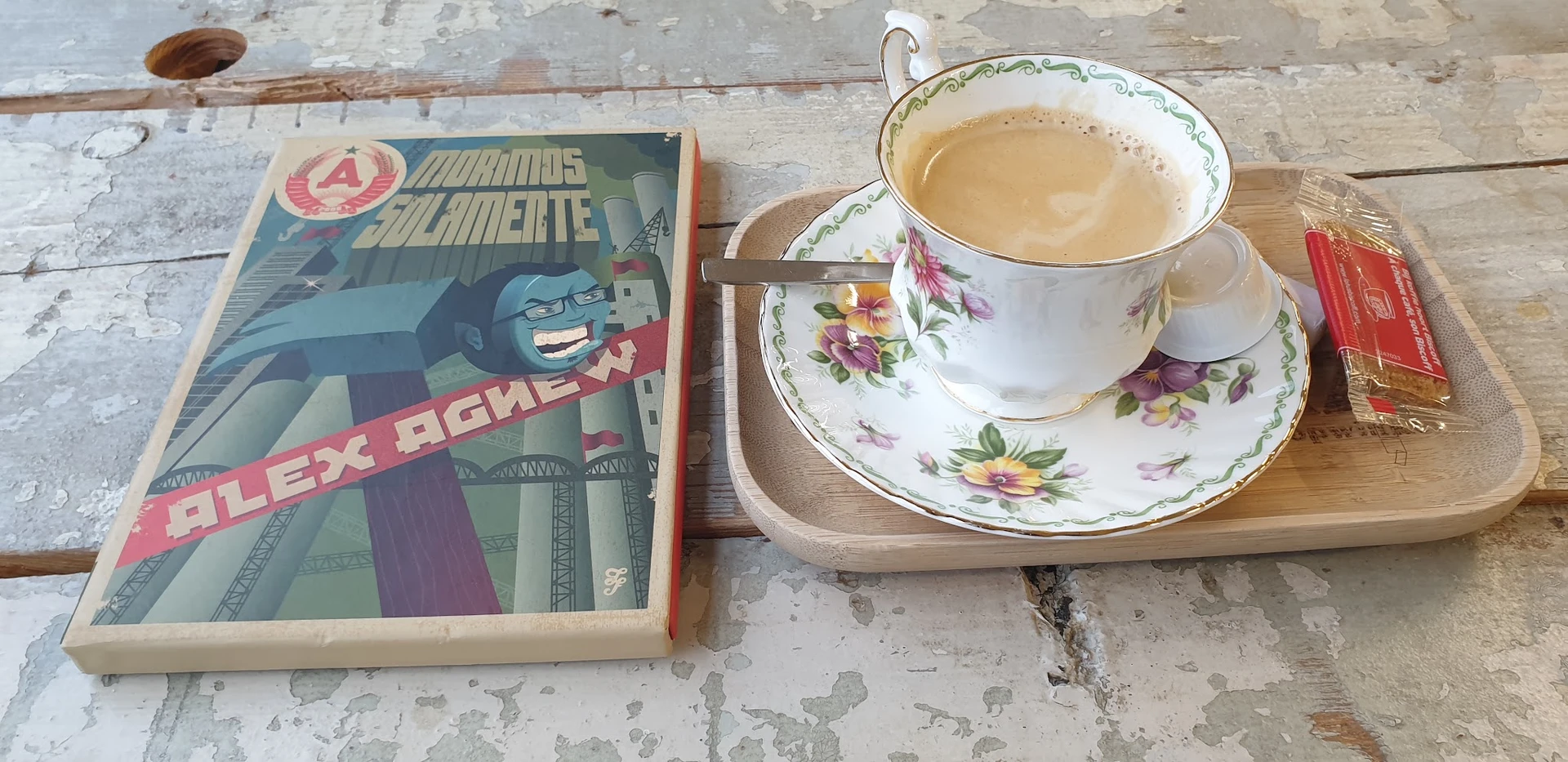 Kopje thee met bloemmotief op schotel naast een Russisch boek op houten tafel