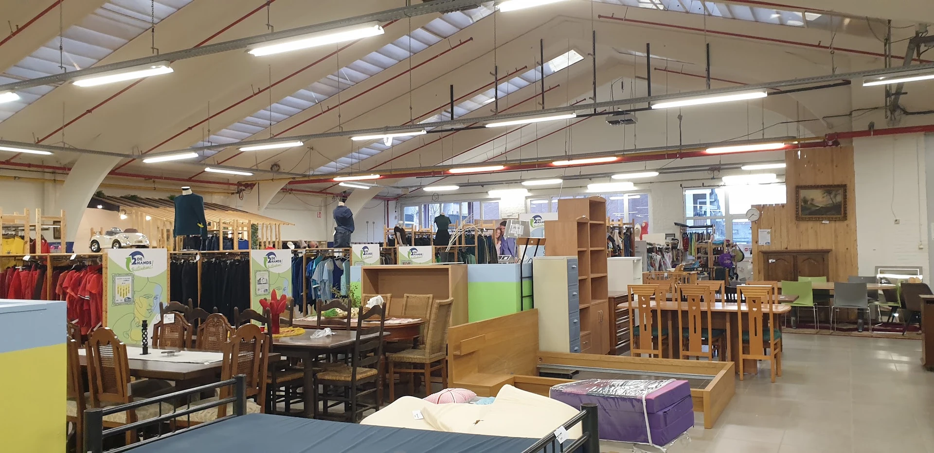 Ruim winkelinterieur met diverse meubels, kledingrekken en stellingen vol tweedehandsartikelen