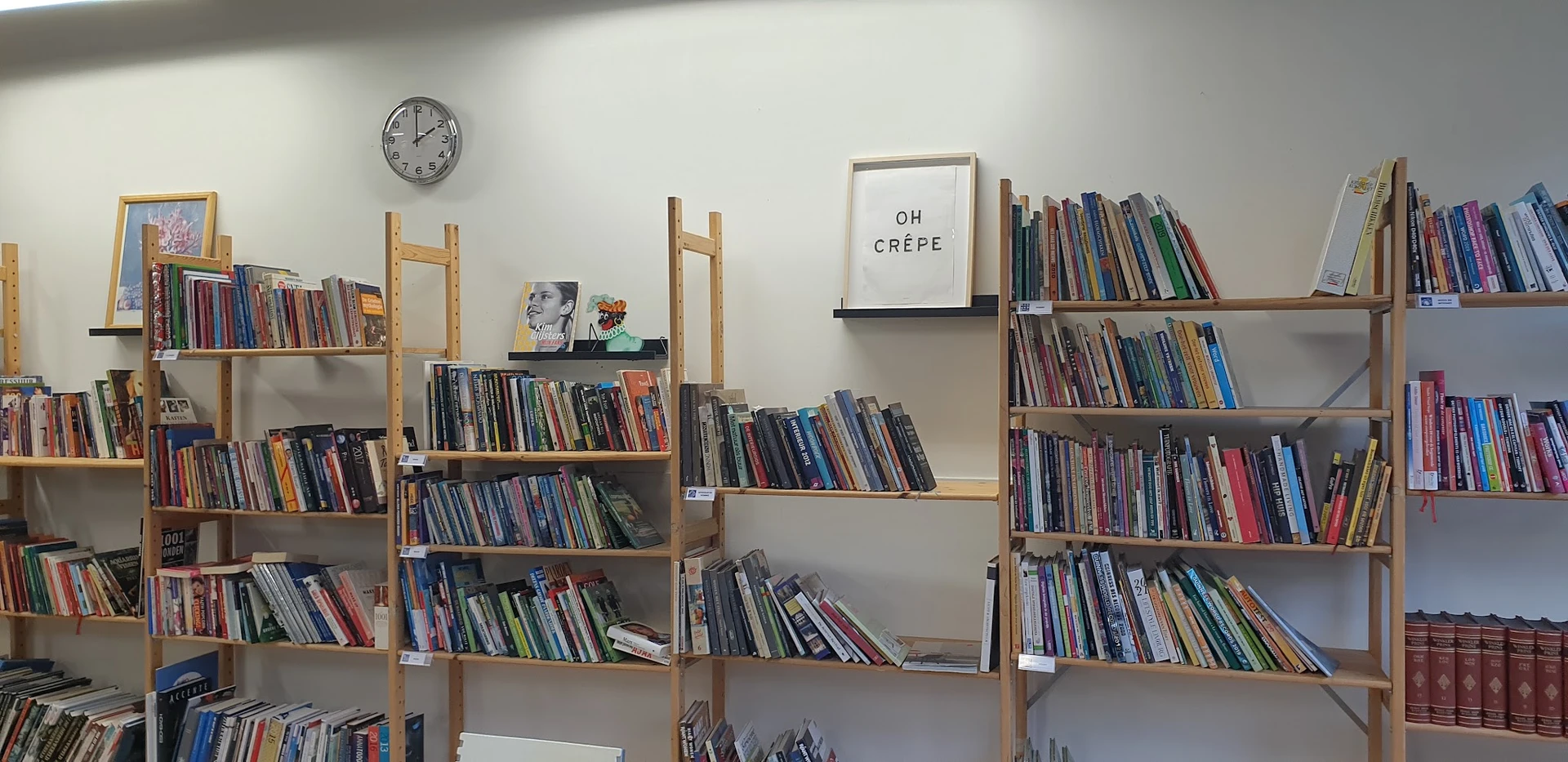 Houten boekenkasten gevuld met tweedehands cd's en dvd's, met klok en decoratief bordje aan de muur.