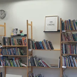 Houten boekenkasten gevuld met tweedehands cd's en dvd's, met klok en decoratief bordje aan de muur.
