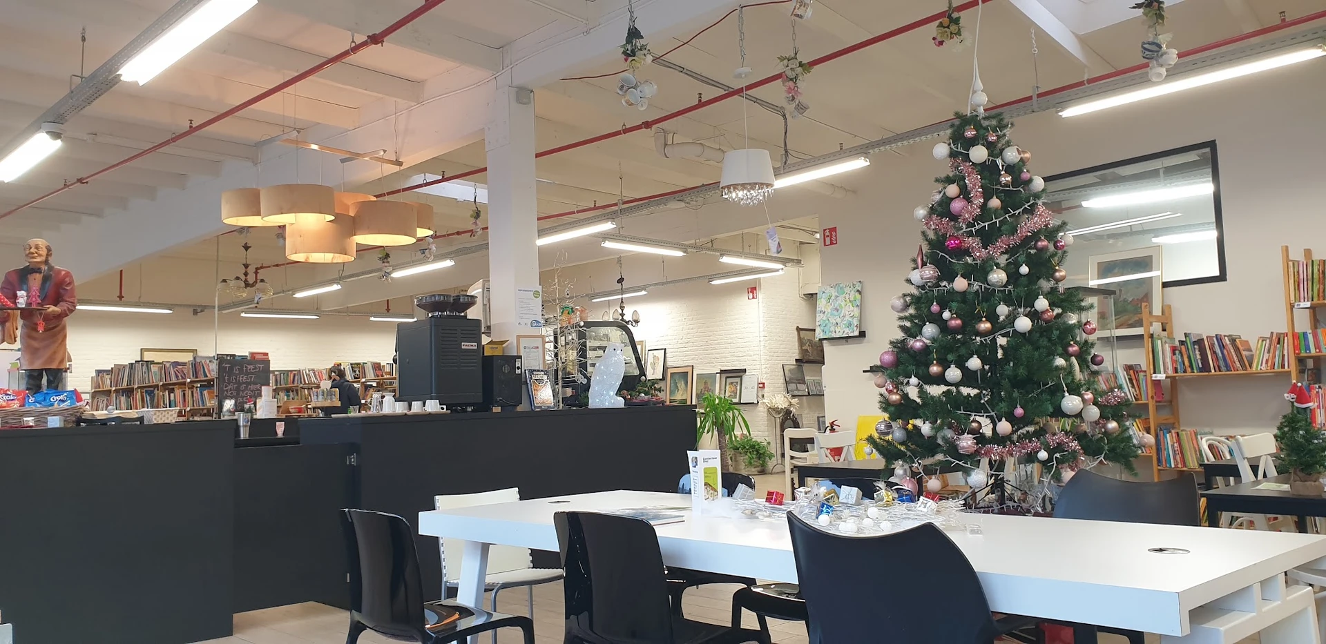 Winkelbinnenkant met zwart bureau, zwarte stoelen, witte tafel, kerstboom met roze en witte versieringen, hanglampen en stell
