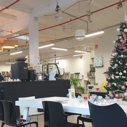 Winkelbinnenkant met zwart bureau, zwarte stoelen, witte tafel, kerstboom met roze en witte versieringen, hanglampen en stell