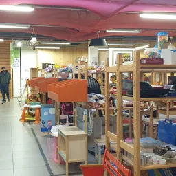Winkelvloer van kringloopwinkel met houten stellingen vol spullen, toonbank en klanten in het achtergrond